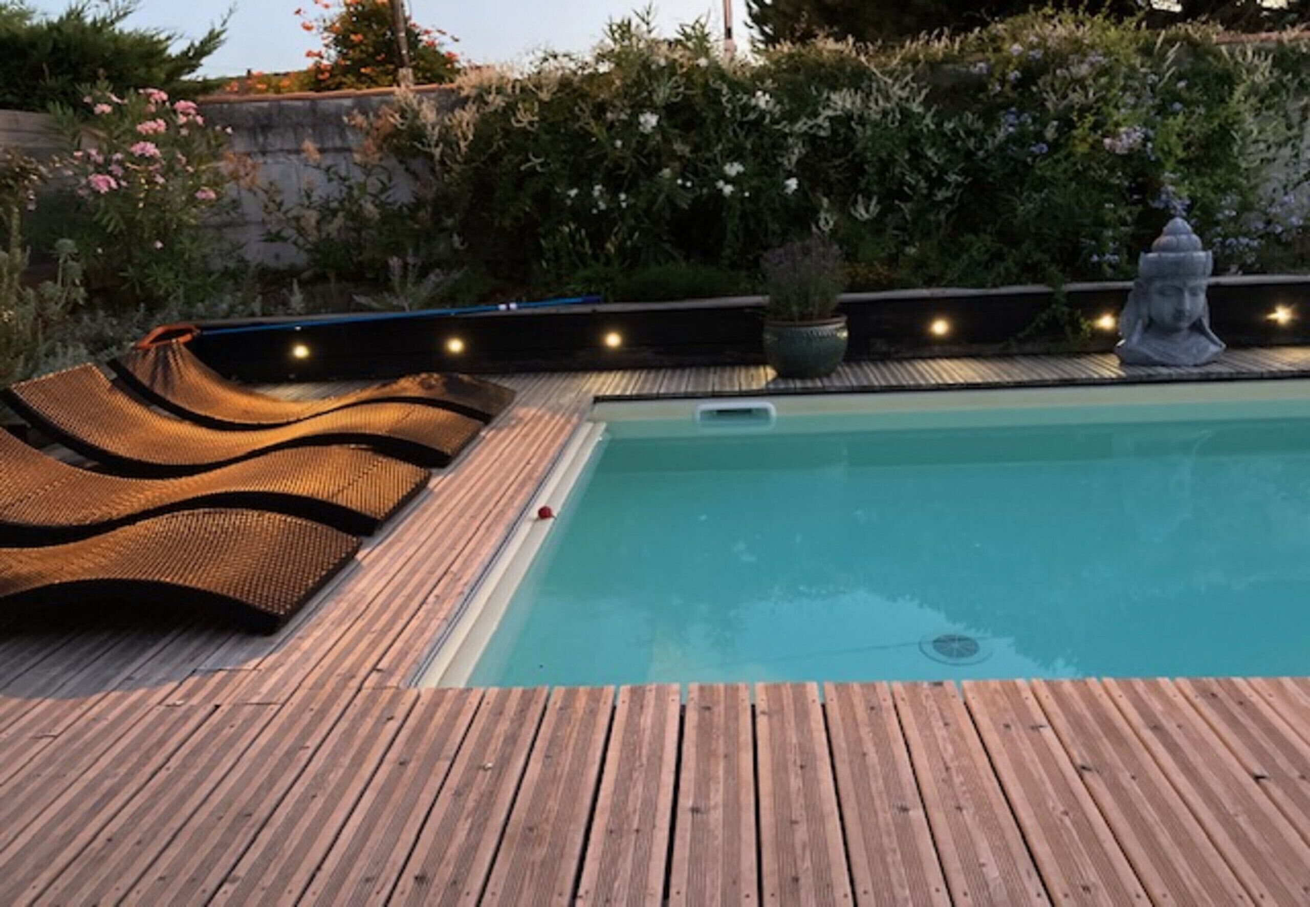 A wooden deck with a swimming pool, surrounded by potted plants and a stone statue.