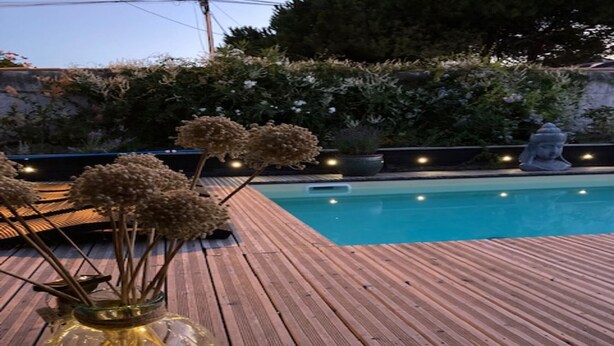 A wooden deck with a pool, surrounded by greenery and decorative lights. - E Villa Clara, 600m de la mer, piscine (Saint-Denis-d´Oléron)