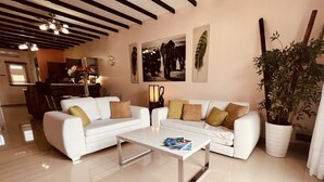 A spacious living room with a white sofa set, a coffee table, and a large potted plant.
