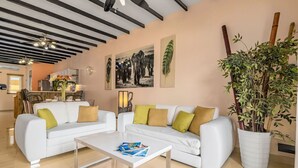 A modern living room with two white sofas, a coffee table, and a large potted plant.