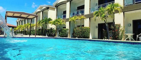 A hotel with a swimming pool, palm trees, and a covered area.