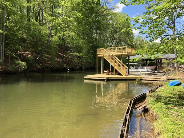 A wooden dock with a staircase leading to a platform, surrounded by lush greenery and a calm body of water.
