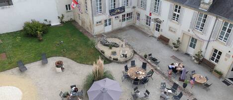 An outdoor courtyard with multiple seating areas, a central garden, and a building with a sign reading "BAR LE DOG".