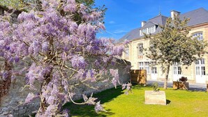 Um edifício histórico com uma parede de pedra e um jardim com glicínias roxas.