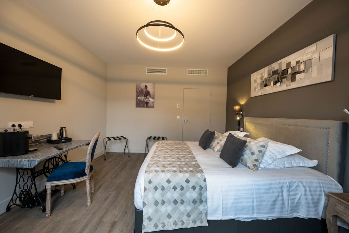 Habitación de hotel con una cama, un escritorio con silla, un televisor y obras de arte en las paredes.