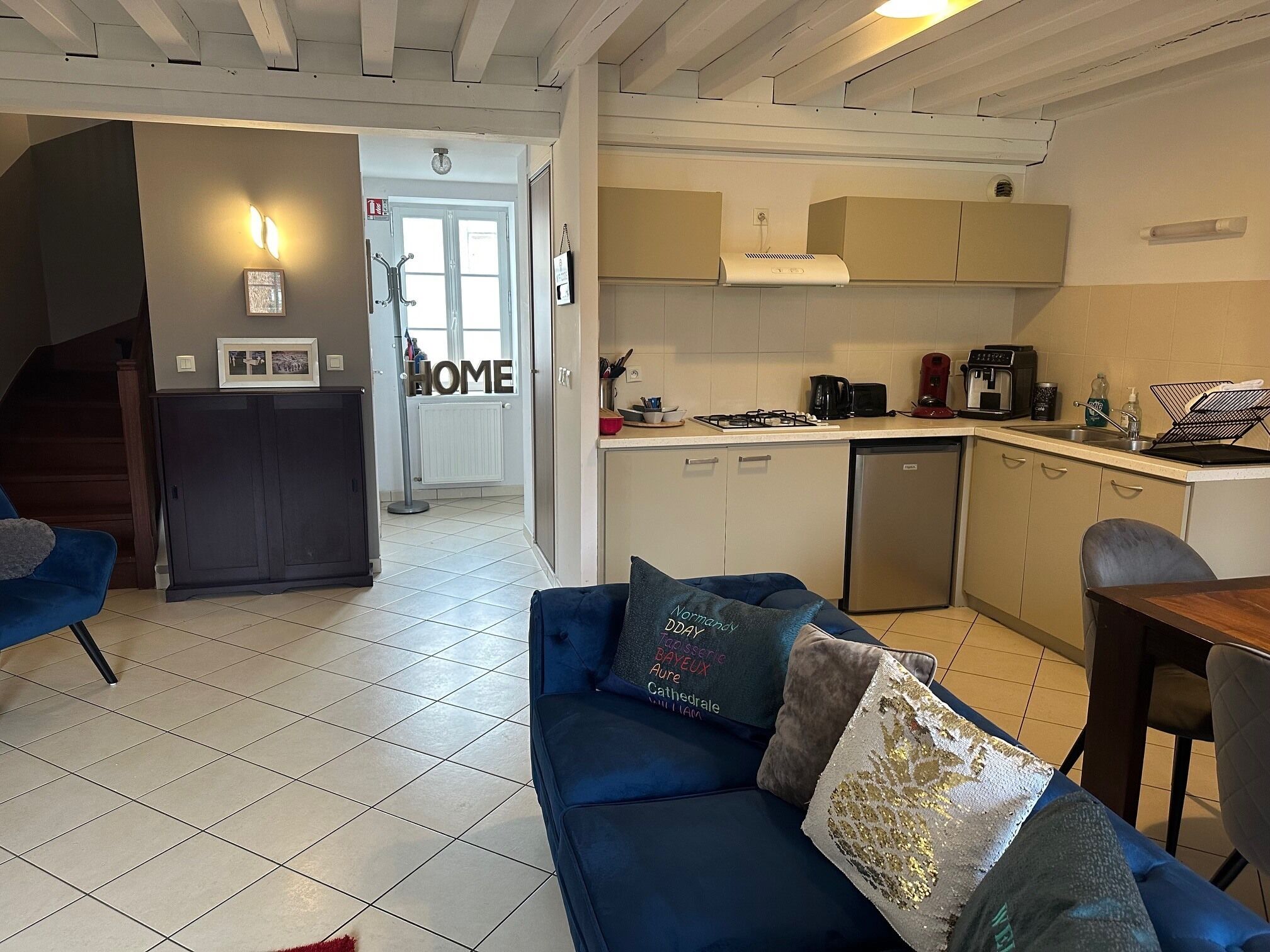 Une cuisine moderne avec des meubles blancs, un lave-vaisselle et une cuisinière. Le salon est doté d’un canapé bleu agrémenté de coussins décoratifs.