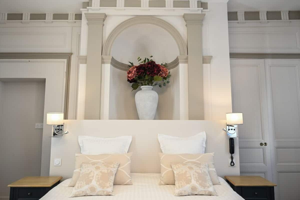 Una habitación de hotel con una cama, dos mesitas de noche, un jarrón con flores y un teléfono en la pared.