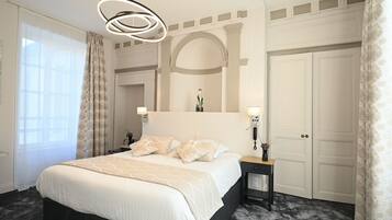 Habitación de hotel con una cama grande, una mesita de noche con lámpara, un espejo sobre la cama y un armario.