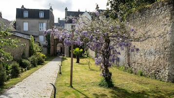 A cobblestone pathway leading to a stone wall with purple flowering trees.