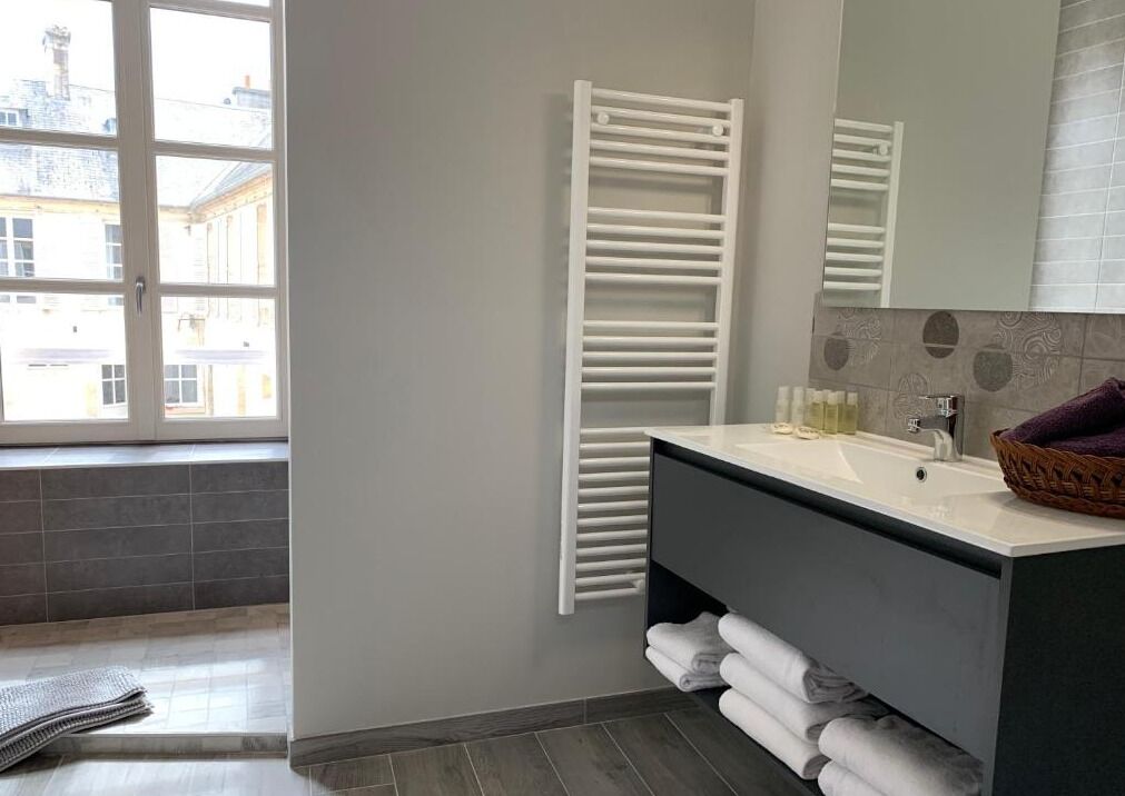 A modern bathroom with a large window, a white towel rack, a dark vanity, and a mirror.