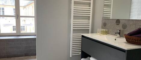 A modern bathroom with a large window, a white towel rack, a dark vanity, and a mirror.