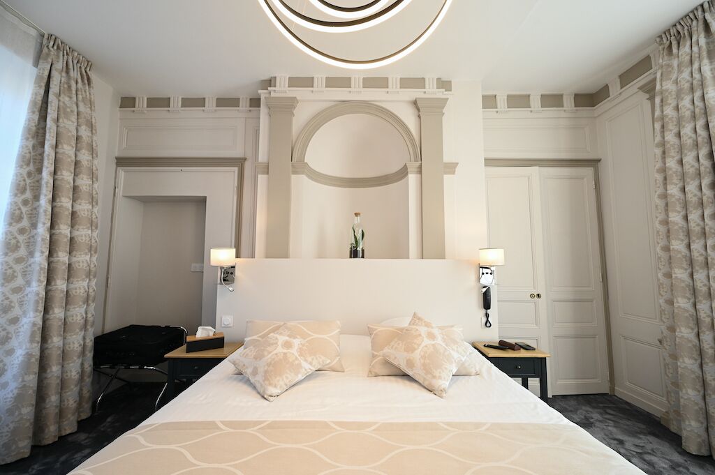 A hotel room with a large bed, two bedside lamps, a desk, and a chair.
