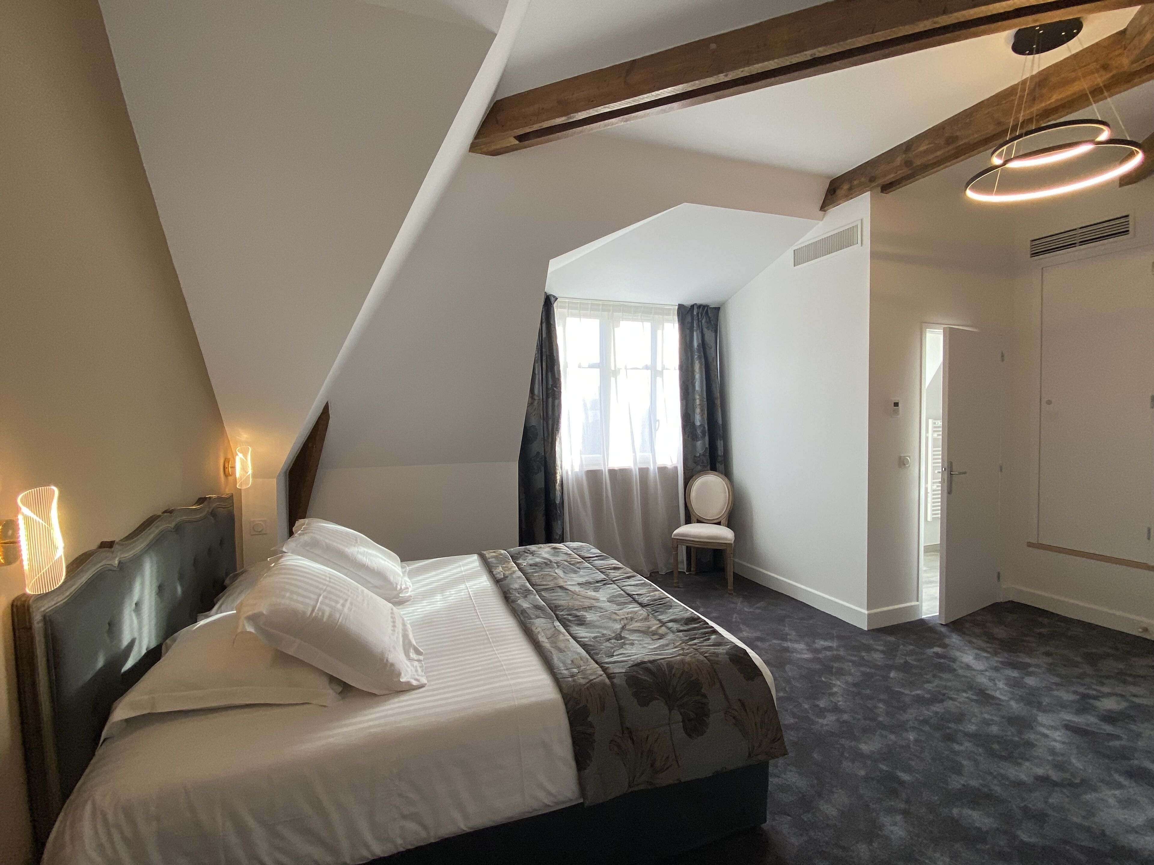 A bedroom with a bed, a chair, a window with curtains, a door, and a ceiling light fixture.