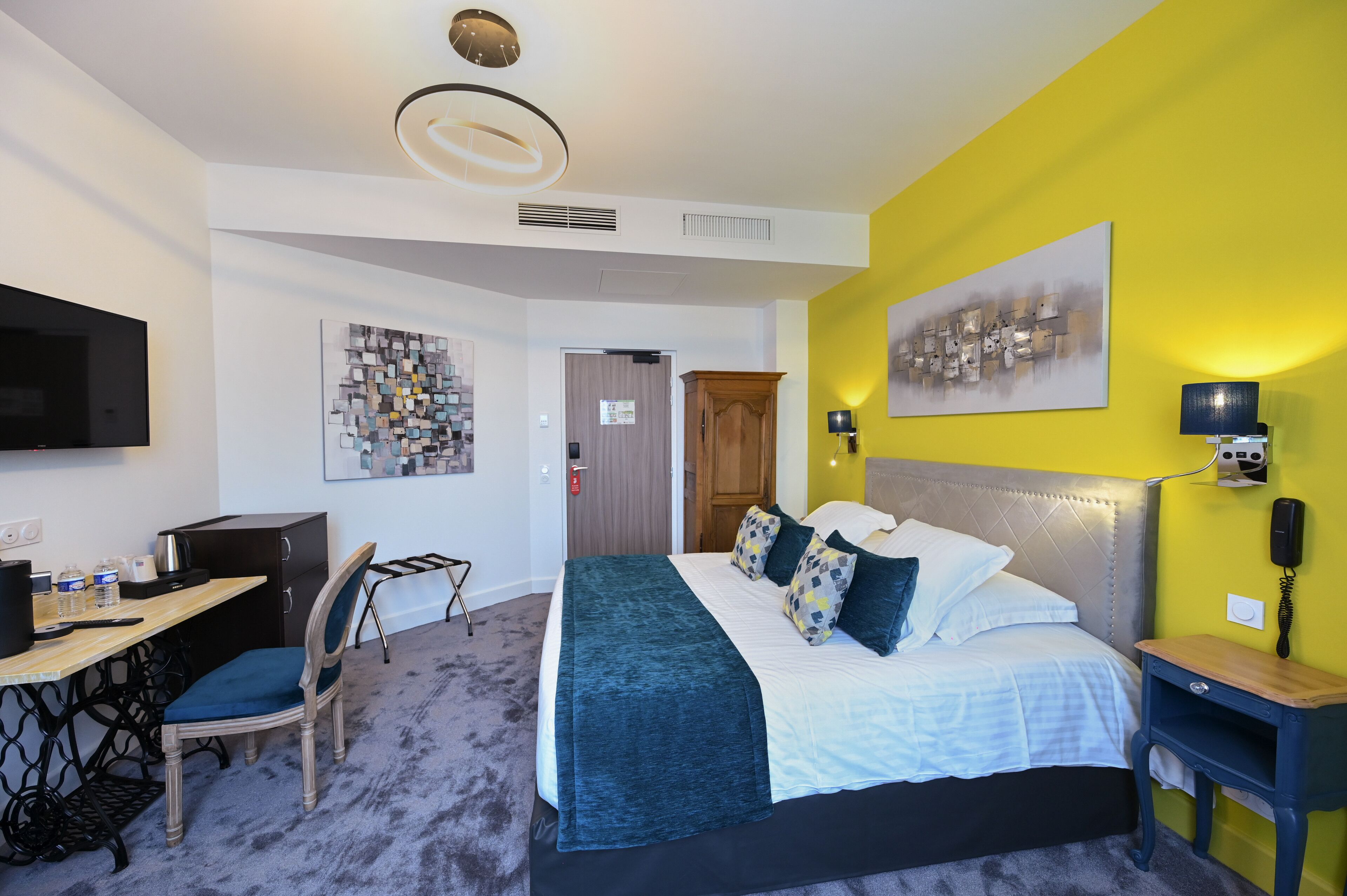 A hotel room with a bed, desk, chair, and artwork on the walls.