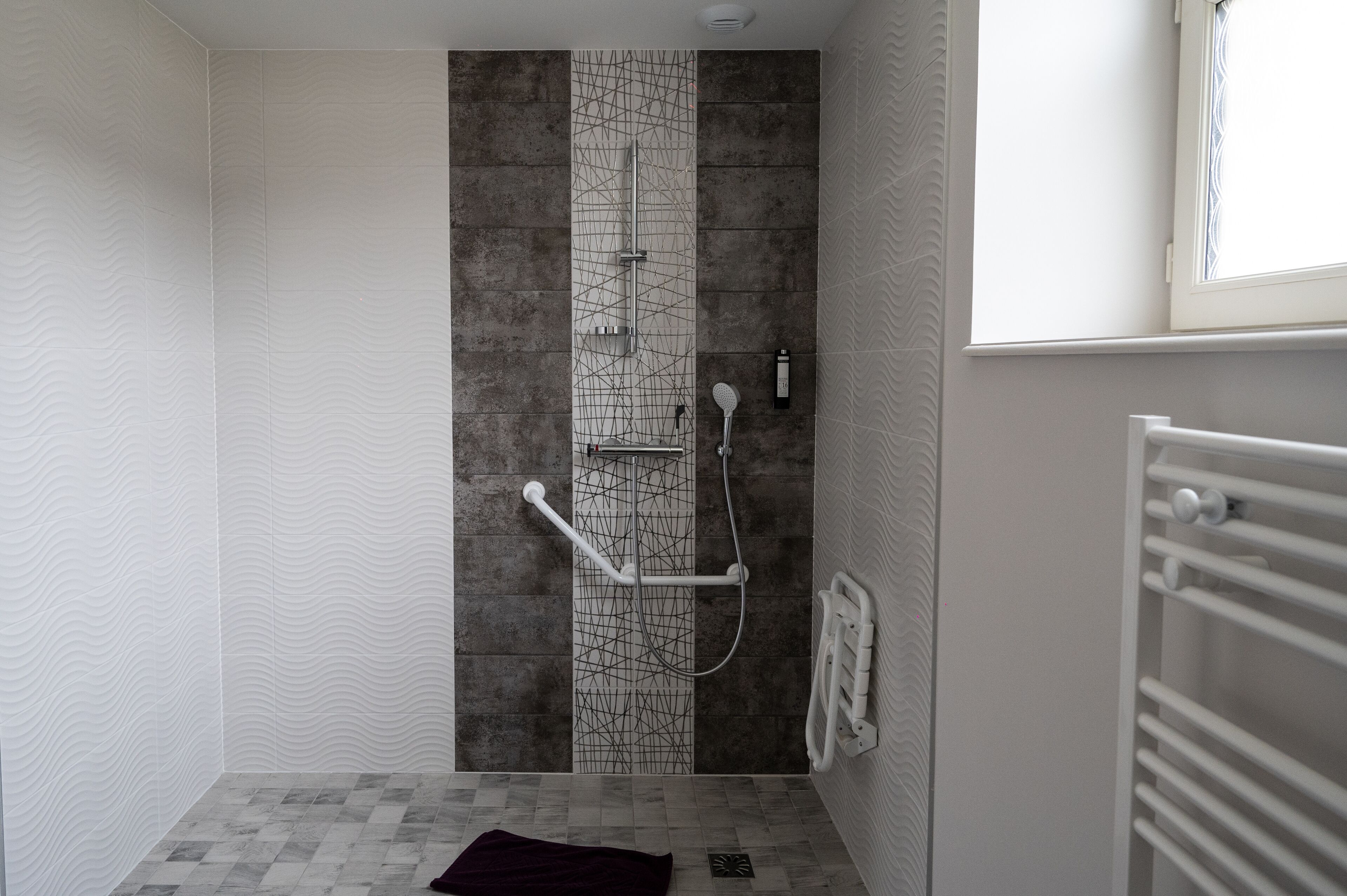 Un espace douche au design moderne, comprenant un mur texturé, un panneau vertical orné d’un motif géométrique et une pomme de douche blanche.