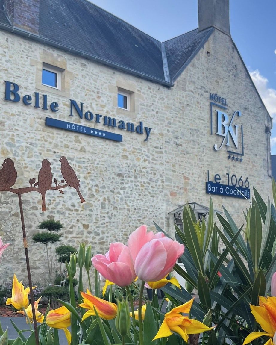 A stone building with signs for 'Belle Normandy Hotel' and 'Le 1066 Bar à Cocktails'.