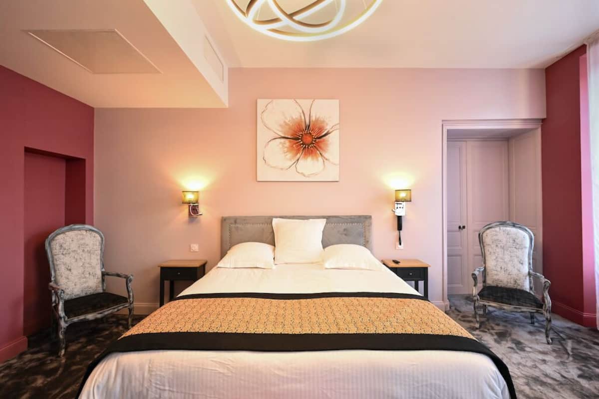 Habitación de hotel con una cama grande, dos mesitas de noche, dos lámparas de pared y un adorno mural.