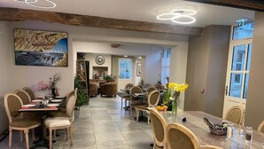 Uma sala de jantar com várias mesas e cadeiras, um quadro grande na parede e vista para o corredor.