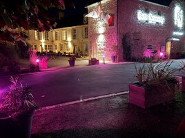 Fachada de hotel de piedra, con mobiliario exterior e iluminación de señalización.