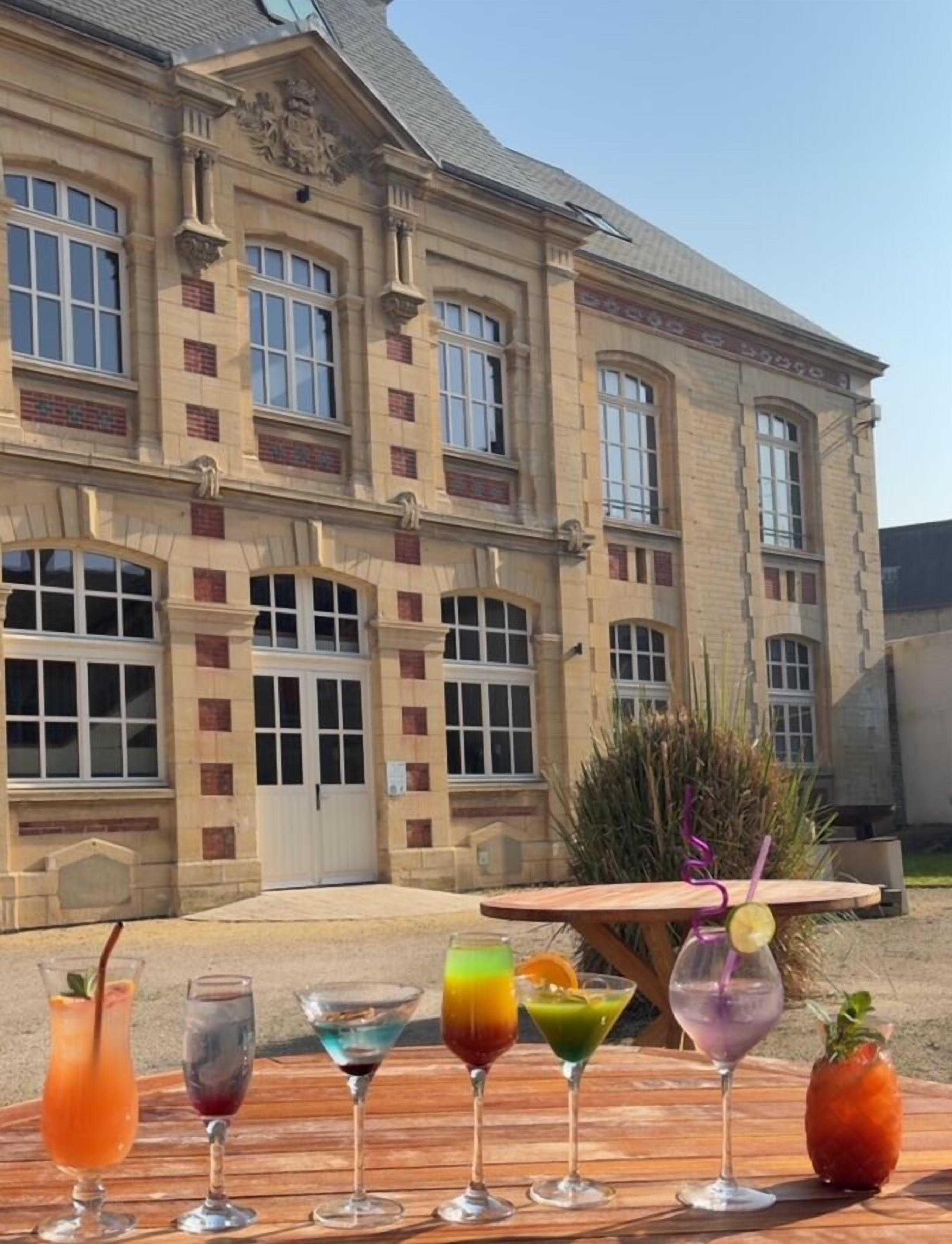 Un edificio con grandes ventanales y una mesa de madera con diversas bebidas.