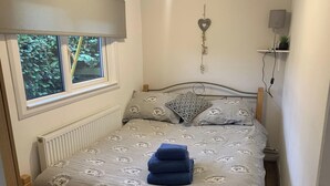 Een slaapkamer met een bed, een radiator, een raam, een hartvormige decoratie aan de muur, en een klein plankje met een plantje.