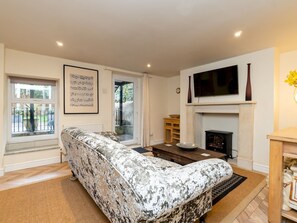A living room with a patterned sofa, a fireplace, a television, and a window with a view of the outdoors.