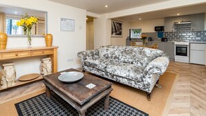 A living room with a sofa, a coffee table, and a dining area with a table and chairs. There is a kitchen in the background with appliances and a window. - Lovely 1 bed apartment with free parking - Pass the Keys (Bath)
