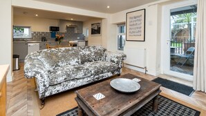 A living room with a patterned sofa, a wooden coffee table, and a kitchen in the background. - Lovely 1 bed apartment with free parking - Pass the Keys (Bath)