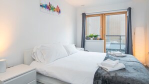 Una habitación de hotel moderna con una cama, una mesita de noche, una ventana con cortinas y un cuadro de un paisaje urbano en la pared.