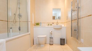 Un baño moderno con ducha de vidrio, inodoro blanco, lavamanos con espejo y toallero.