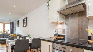 Una cocina moderna con electrodomésticos de acero inoxidable, un comedor con mesa y sillas, y una sala de estar con sofá y plantas.
