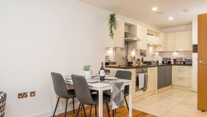 Una cocina moderna con zona de comedor, que incluye una mesa blanca, sillas negras y una planta colgante.