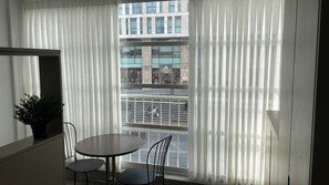 Uma varanda com mesa e cadeiras, um vaso de planta e vista para um prédio com uma placa que diz 'adidas'.
