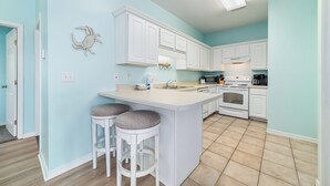 Una cocina con armarios blancos, una isla central con taburetes, un microondas, estufa y un lavaplatos.