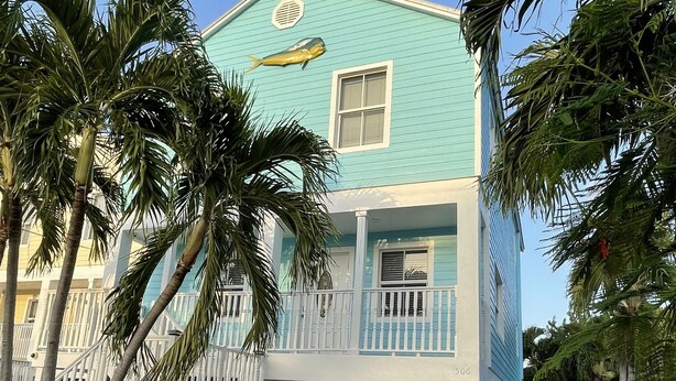 A two-story house with a light blue exterior, a balcony with white railings, and a garage door. - Tropical Retreat in the Heart of the Keys (Marathon)