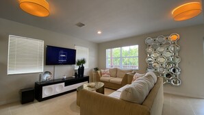 A modern living room with a beige sofa, a TV on the wall, and a decorative mirror. - Tropical Retreat in the Heart of the Keys (Marathon)