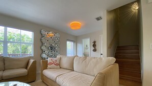 A living room with a beige sofa, a round coffee table, and a decorative wall piece. A staircase is visible in the background. - Tropical Retreat in the Heart of the Keys (Marathon)