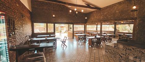 A spacious restaurant with high ceilings, exposed brick walls, and patterned tile flooring. Tables and chairs are arranged for dining.