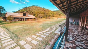 A building with a covered patio area, a grassy lawn, and a hill in the background. - COMPLEXO JARDIM SECRETO (Santa Barbara)