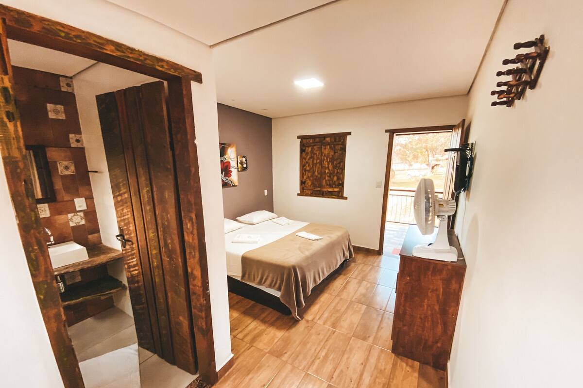 A bedroom with a bed, a bedside table, a window, and a fan.