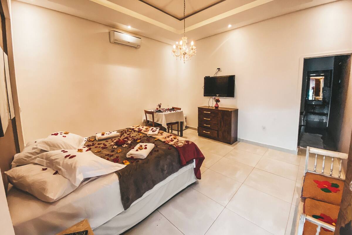 A bedroom with a bed, bedside table, dresser, TV, and a chandelier.