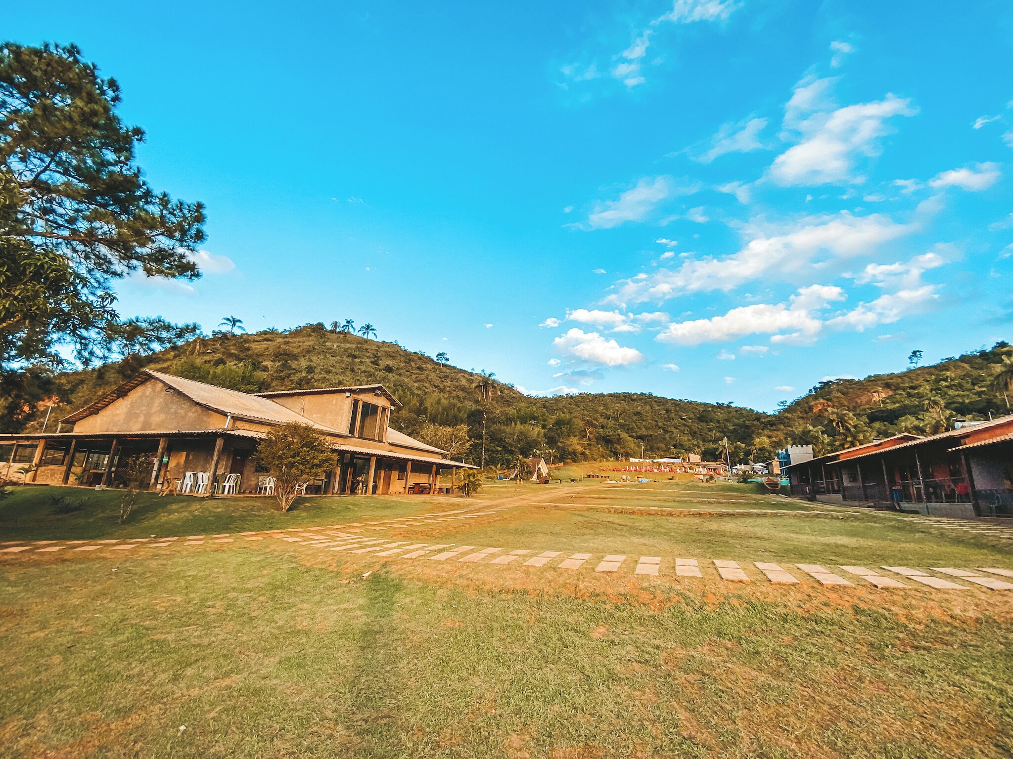 A rural setting with a large open grassy area, a building with a corrugated metal roof, and a hill in the background.