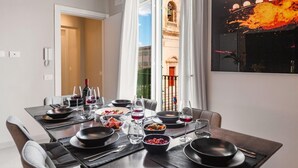 A dining room with a table set for a meal, a view of a building through a window, and a painting on the wall. - Casa San Lio (Noto)