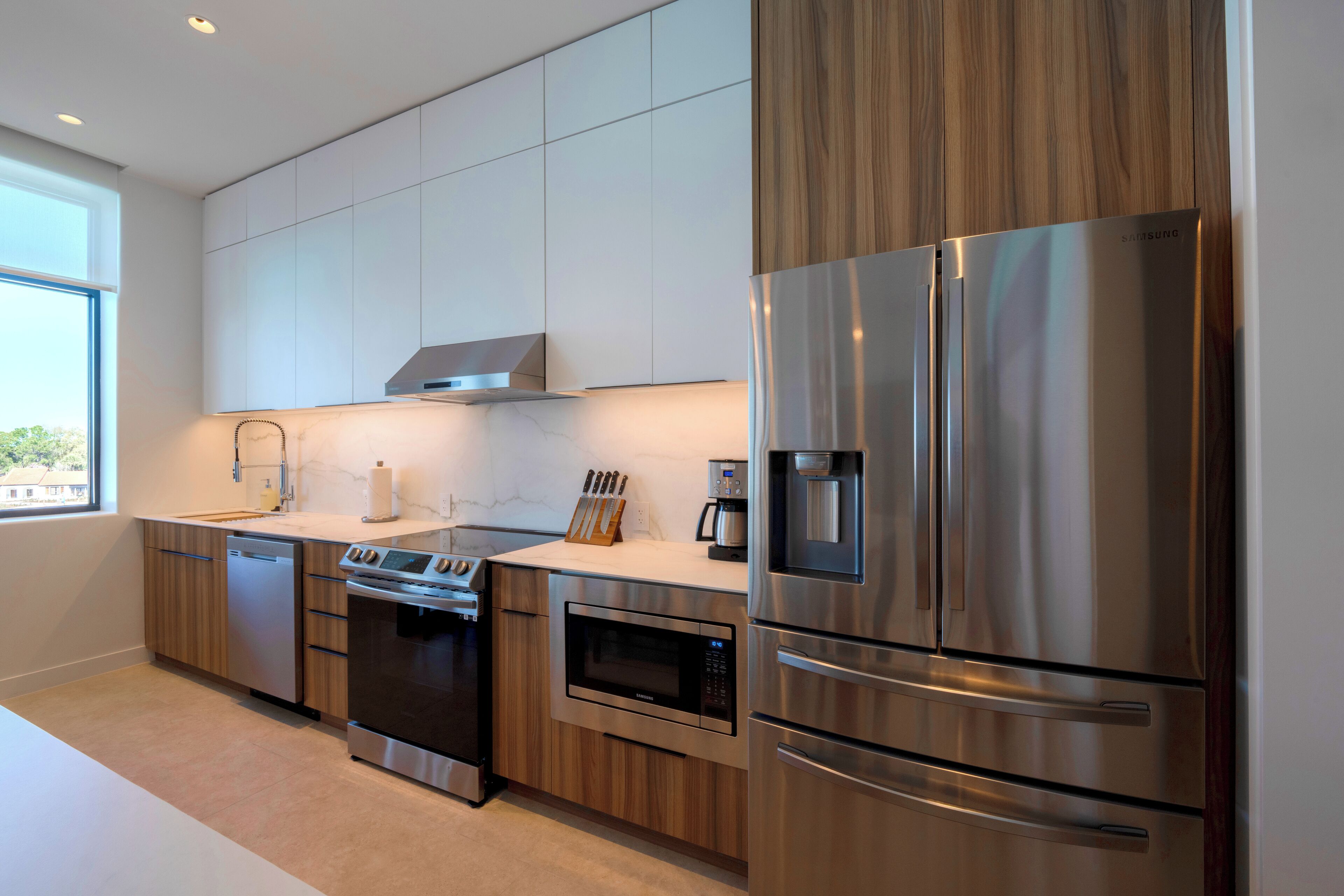 A modern kitchen with stainless steel appliances, wooden cabinets, and a large window providing natural light.