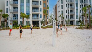 A beach volleyball game in front of a modern hotel with multiple balconies and palm trees. - Evermore Orlando Resort (Orlando)