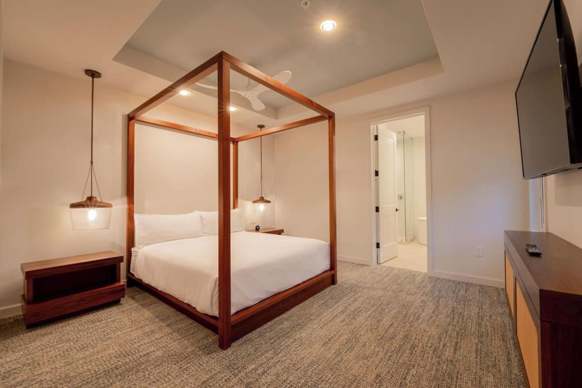 A bedroom with a four-poster bed, a wooden nightstand, a TV, and a ceiling fan.