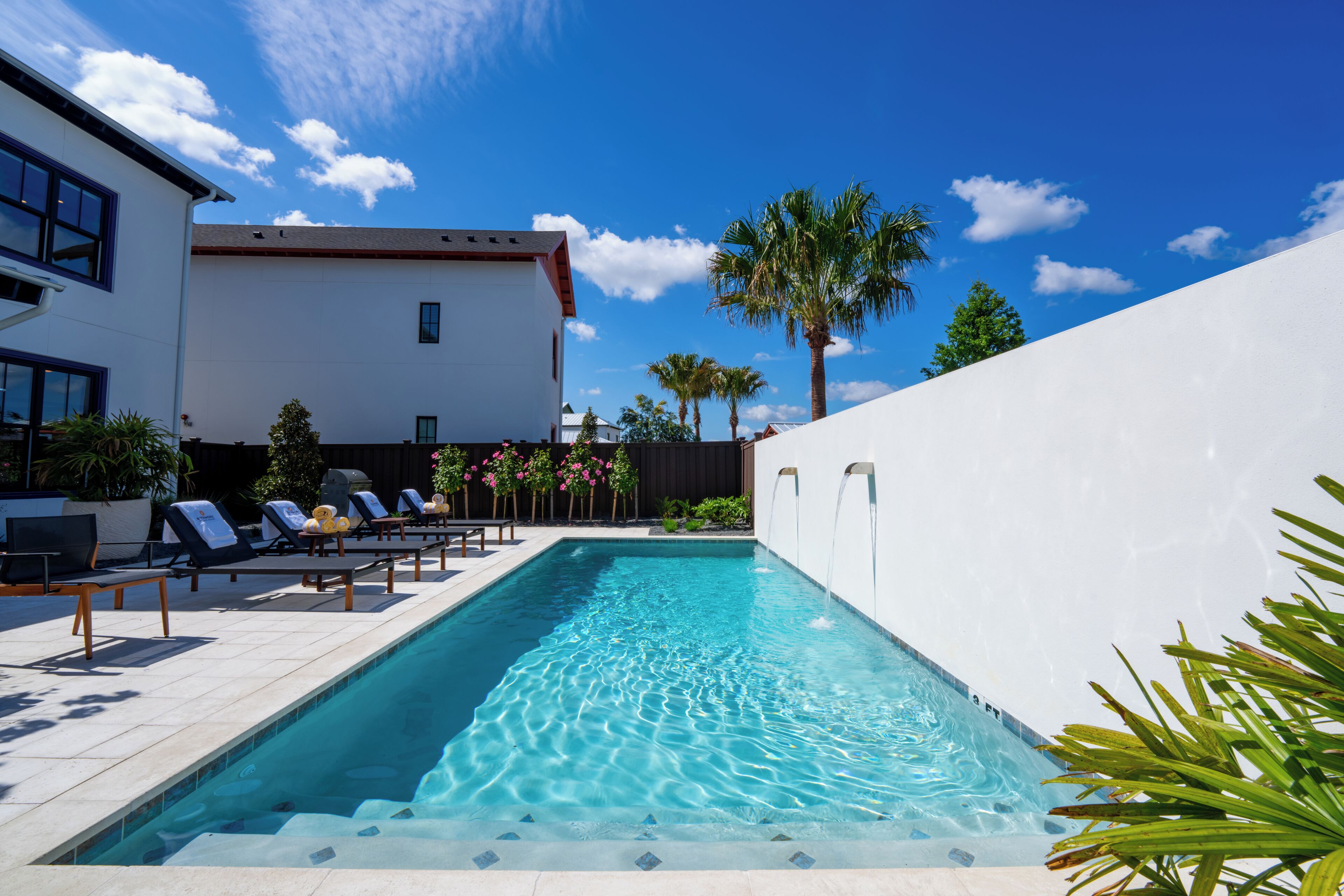 Ein Pool mit Liegestühlen, ein weißes Gebäude und Palmen.