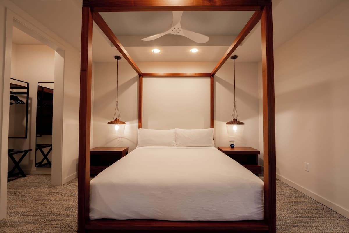 A bedroom with a canopy bed, two bedside tables, a ceiling fan, and a walk-in closet.