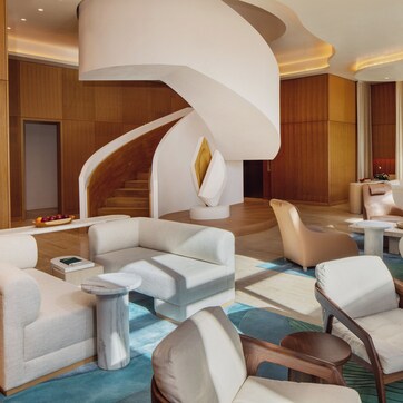 A modern hotel lobby with a curved staircase, plush seating areas, and a wooden finish on the walls.