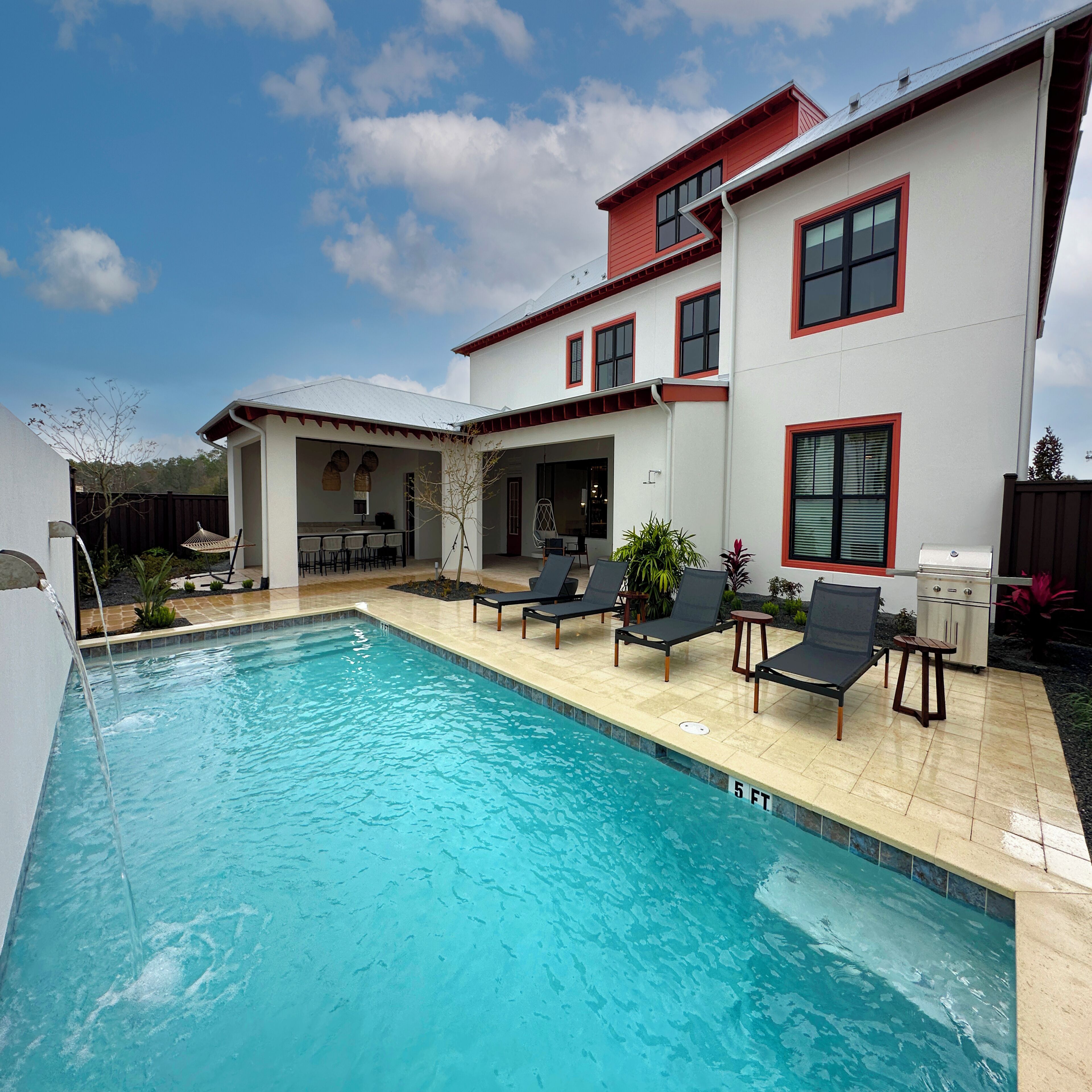 Una piscina con sillas de descanso y zona de barbacoa en un patio trasero.